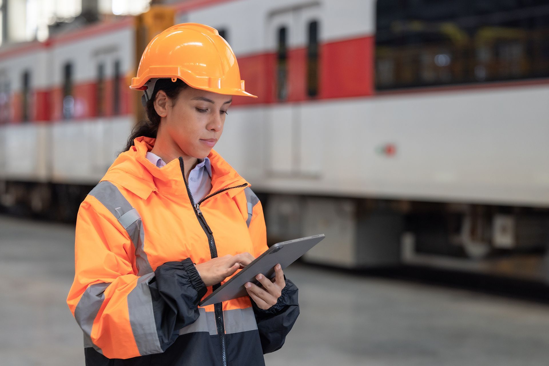 A woman in a hard hat is using a tablet in front of a train.