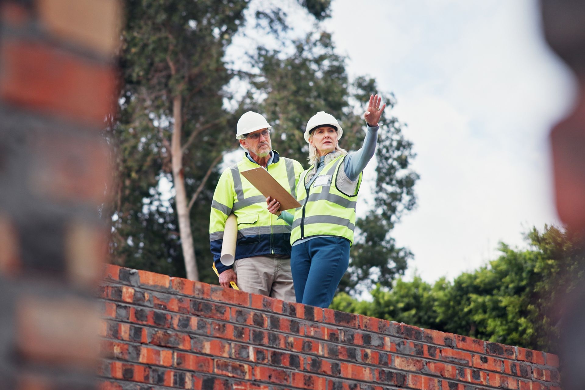 A man and a woman are standing on top of a brick wall.