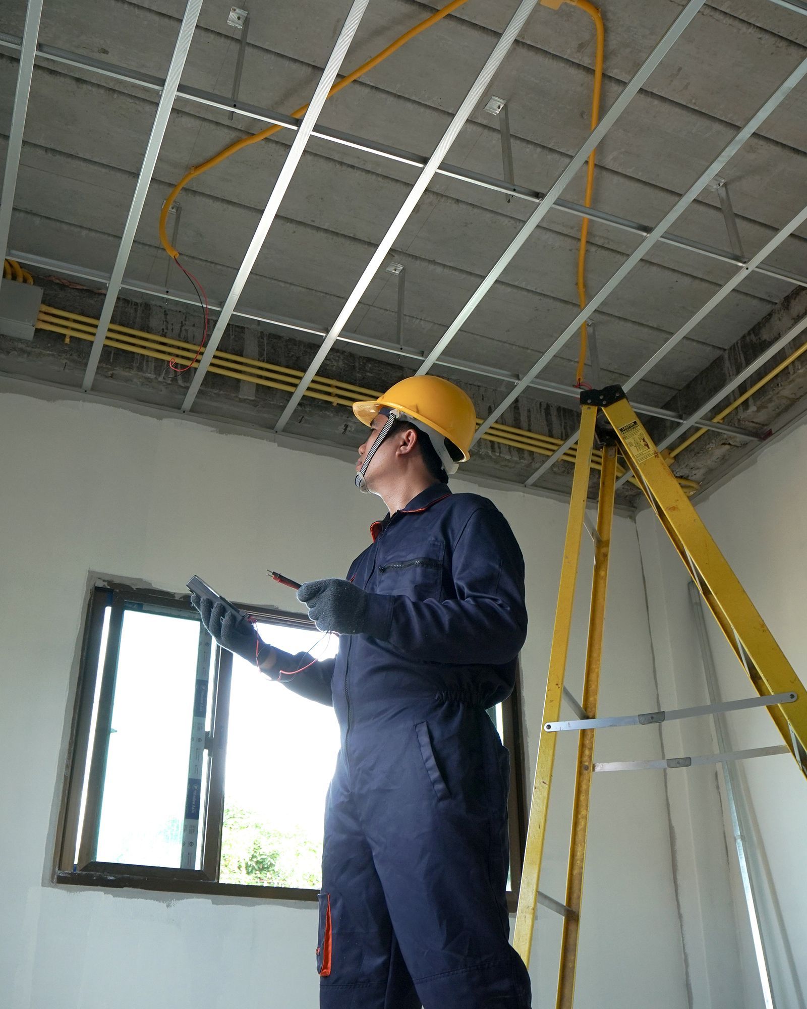 A man is standing on a ladder in a room looking up at the ceiling.