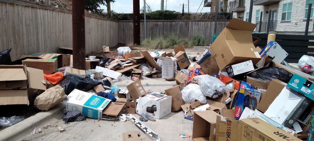 a man is picking up trash on the side of the road in front of a garbage truck .
