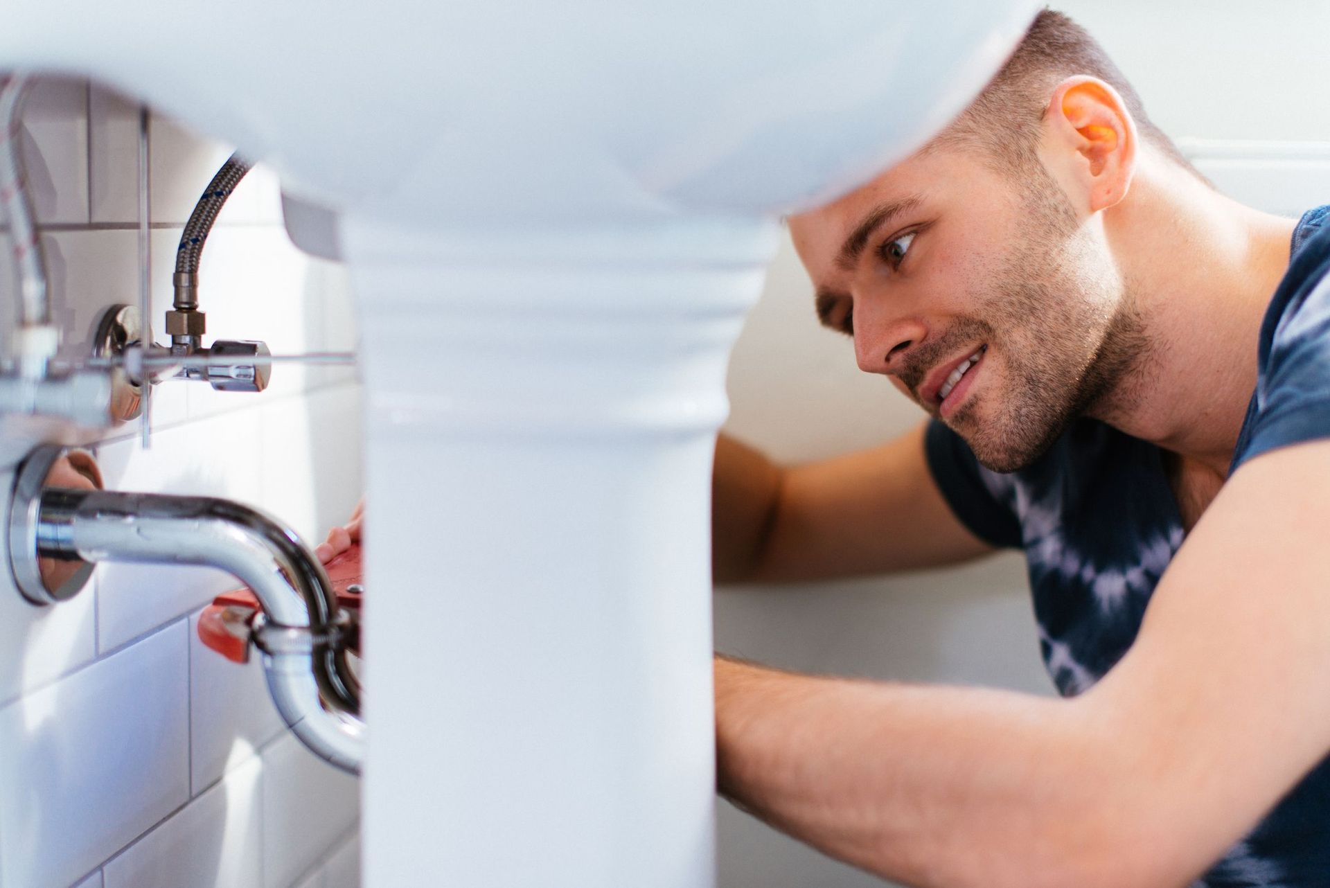 Plumber repairing a sink pipe under a bathroom basin, focused on the plumbing work