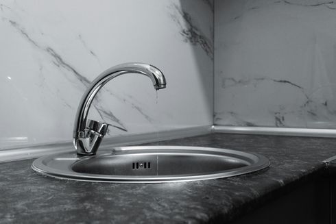 Chrome kitchen faucet over a stainless steel sink on a dark countertop