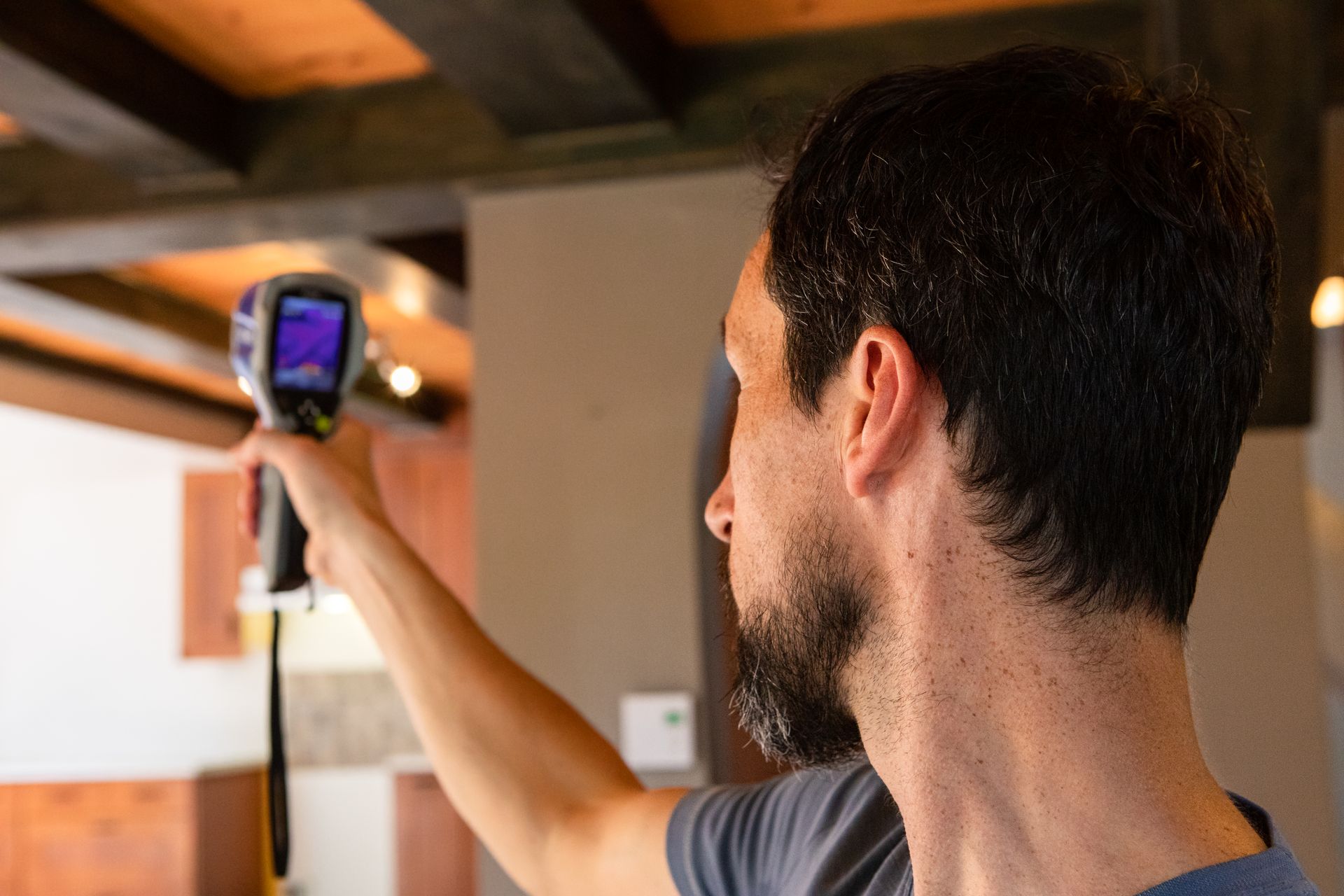 Person using a thermal camera to inspect a ceiling with exposed wooden beams.