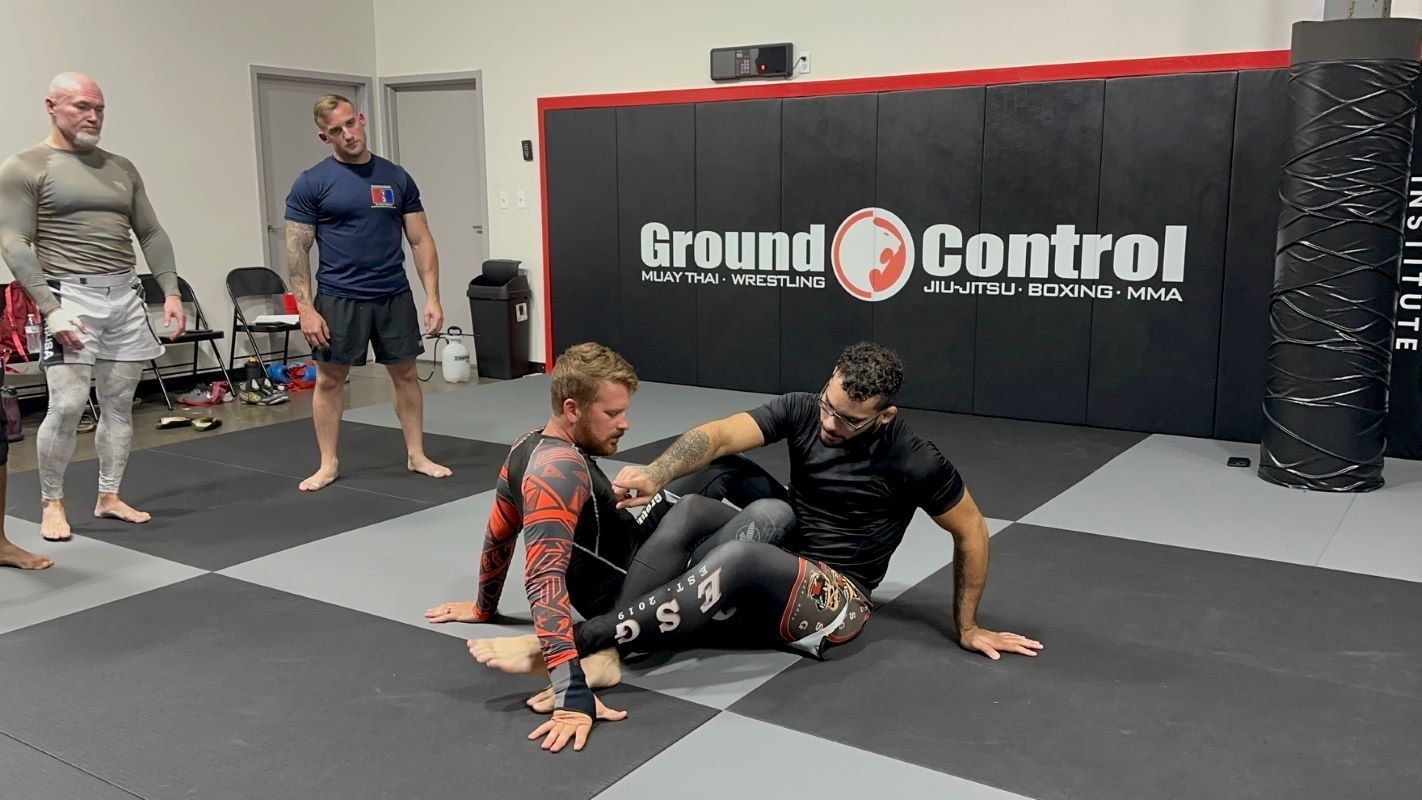 Two men practicing Brazilian Jiu-Jitsu on a mat. One is in a guard position, the other is passing. Ground Control gym.