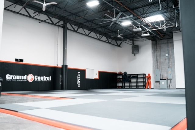Empty martial arts gym with mats, black and orange accents, logo