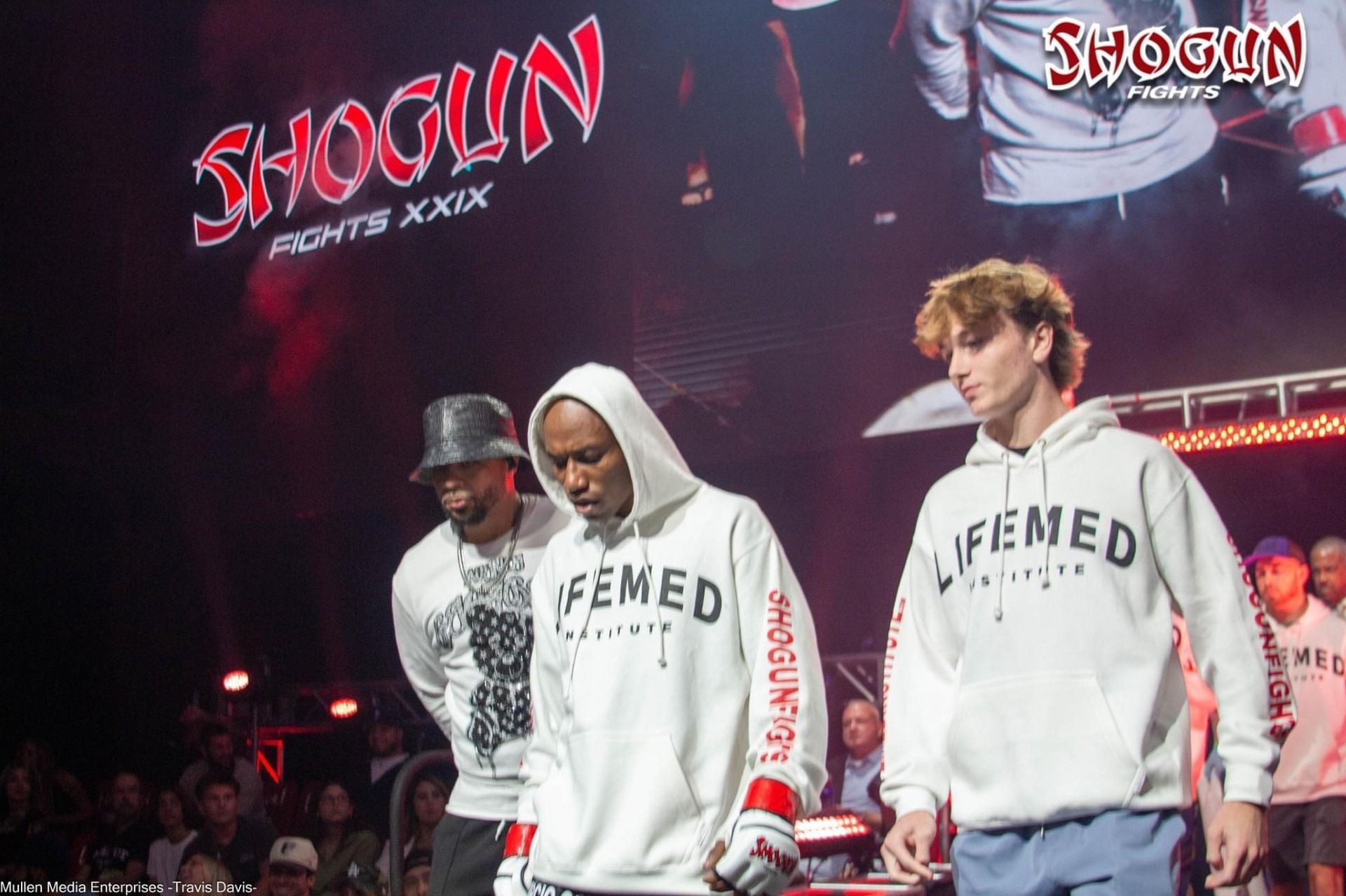 Three men wearing white hoodies at a Shogun Fights event. The hoodies have 