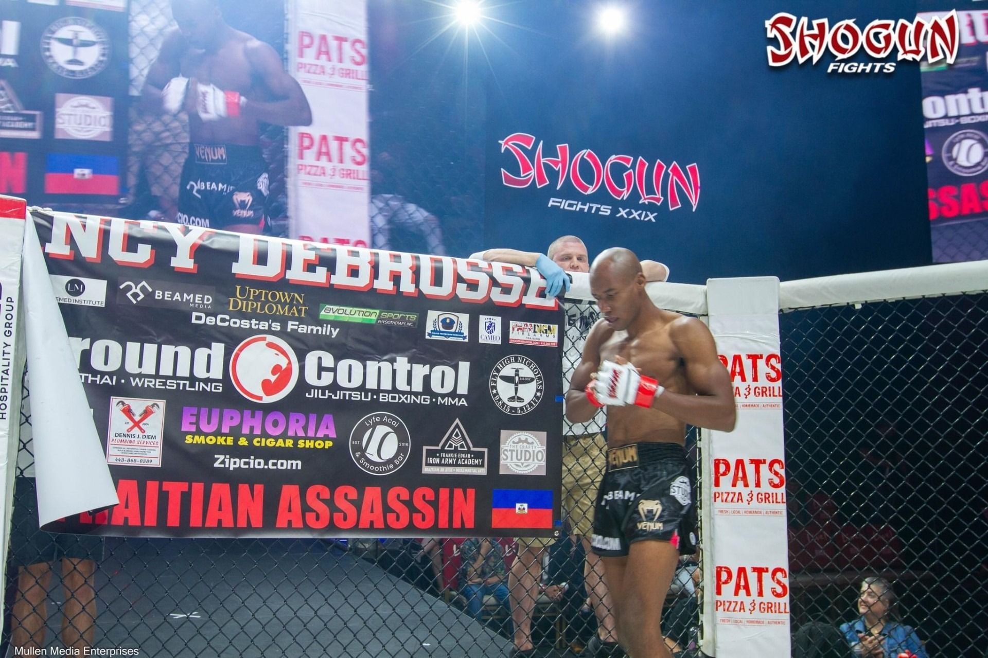 MMA fighter, Quincy Debrosse, in the cage. He wears red gloves and black shorts. Banner says 