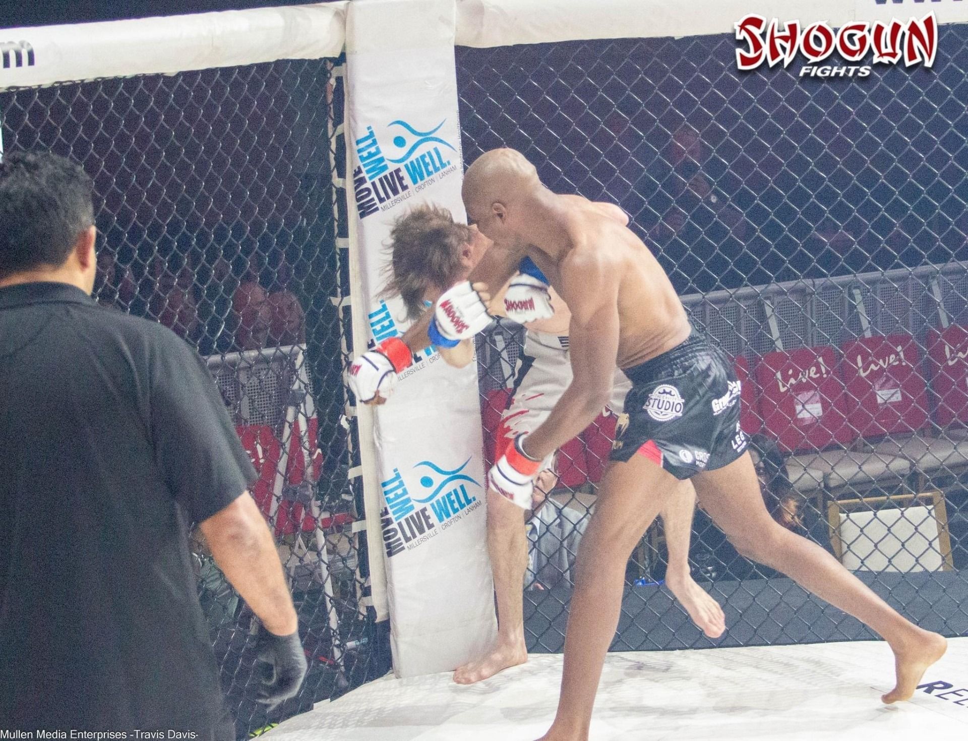 Two MMA fighters in a cage, one shirtless, in a clinch against the wall; referee watches.