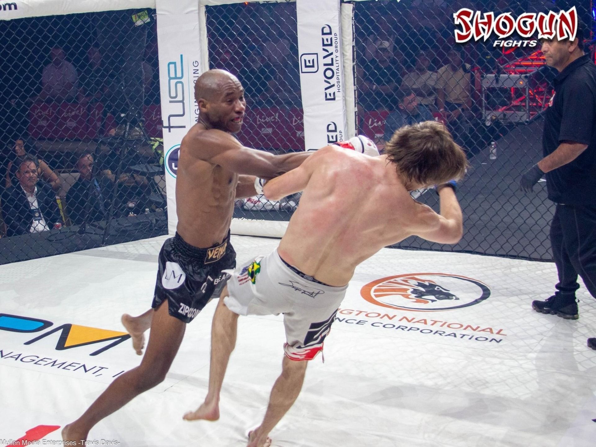 Fighter in black shorts throws a punch at a fighter in white shorts in a cage during a Shogun Fights event.