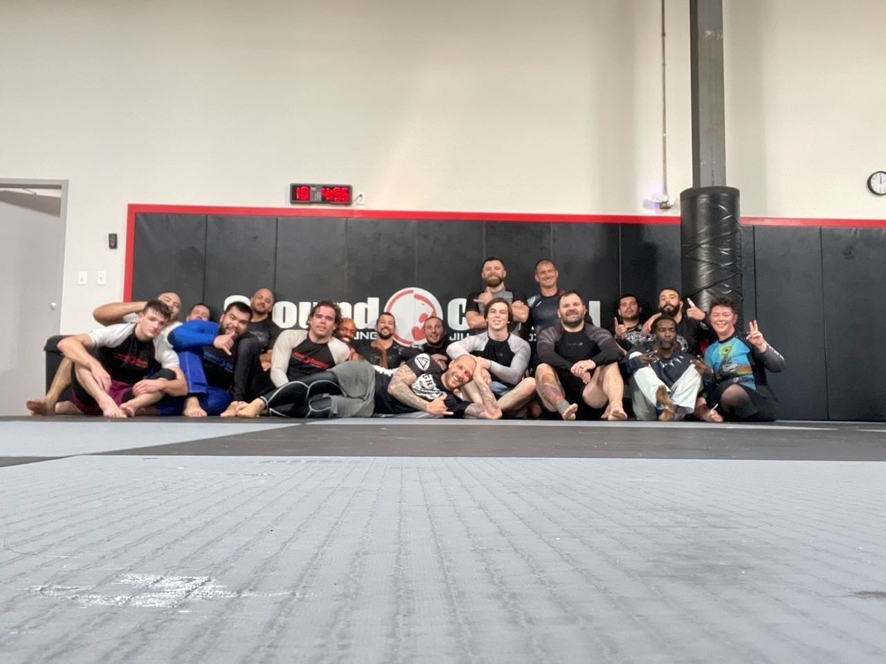 A group of people in workout clothes seated on a mat, posing for a photo.