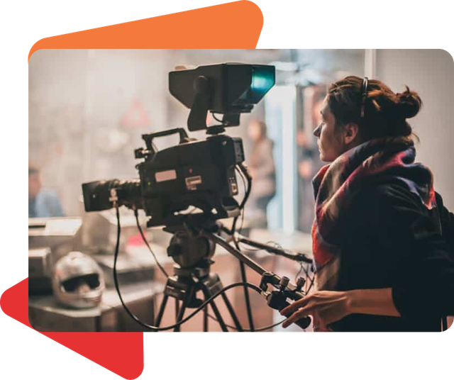 A person wearing a scarf operates a professional video camera on a tripod in a studio setting.