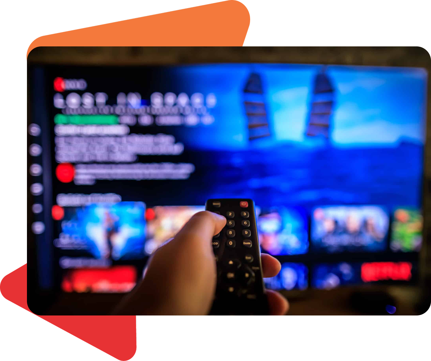 A hand holds a remote control, pointing it at a television screen displaying the Netflix interface for "Lost in Space."