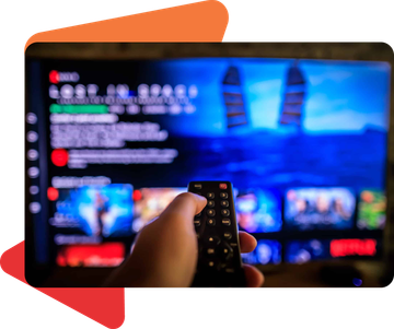 A hand holds a remote control, pointing it at a television screen displaying the Netflix interface for "Lost in Space."