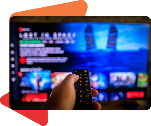 A hand holds a remote control, pointing it at a television screen displaying the Netflix interface for "Lost in Space."