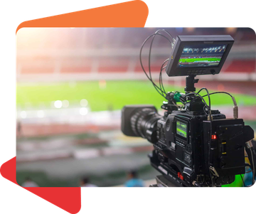 A professional video camera records a stadium field at night, focusing on a monitor displaying the live broadcast.