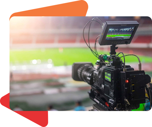 A professional video camera records a stadium field at night, focusing on a monitor displaying the live broadcast.