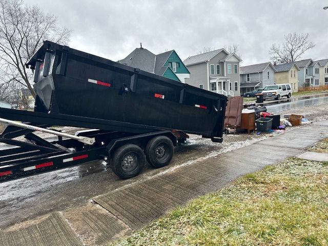 A dumpster is being pulled by a trailer down a street.