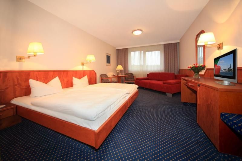 Ein Hotelzimmer mit Bett, Couch, Schreibtisch und Fernseher.