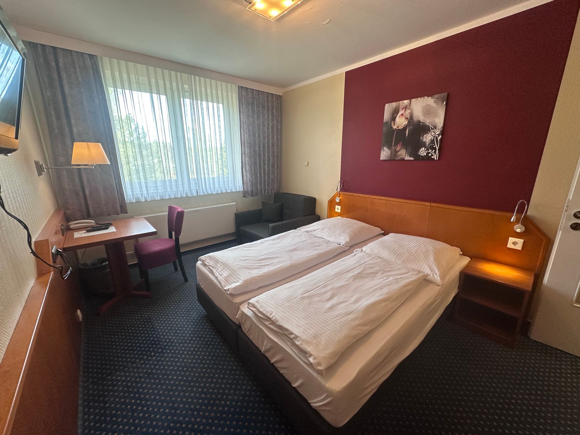 Ein Hotelzimmer mit zwei Betten, einem Stuhl, einem Schreibtisch und einem Fernseher.