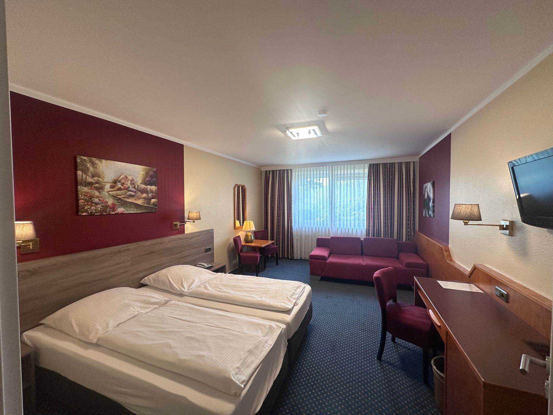 Ein Hotelzimmer mit zwei Betten, einer Couch, einem Schreibtisch und einem Fernseher.