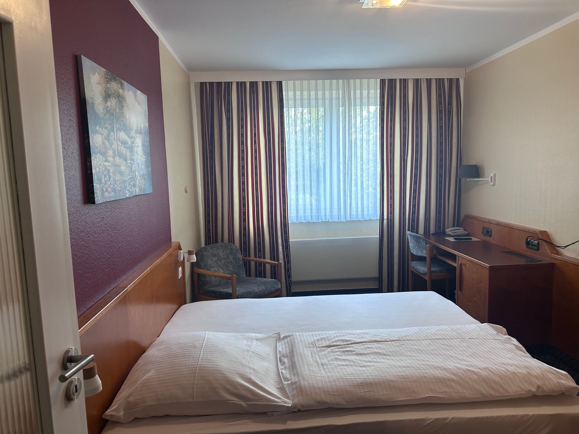 Ein Hotelzimmer mit Bett, Schreibtisch, Stuhl und Fenster.