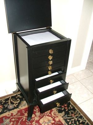 A black jewelry box with gold knobs sits on a rug