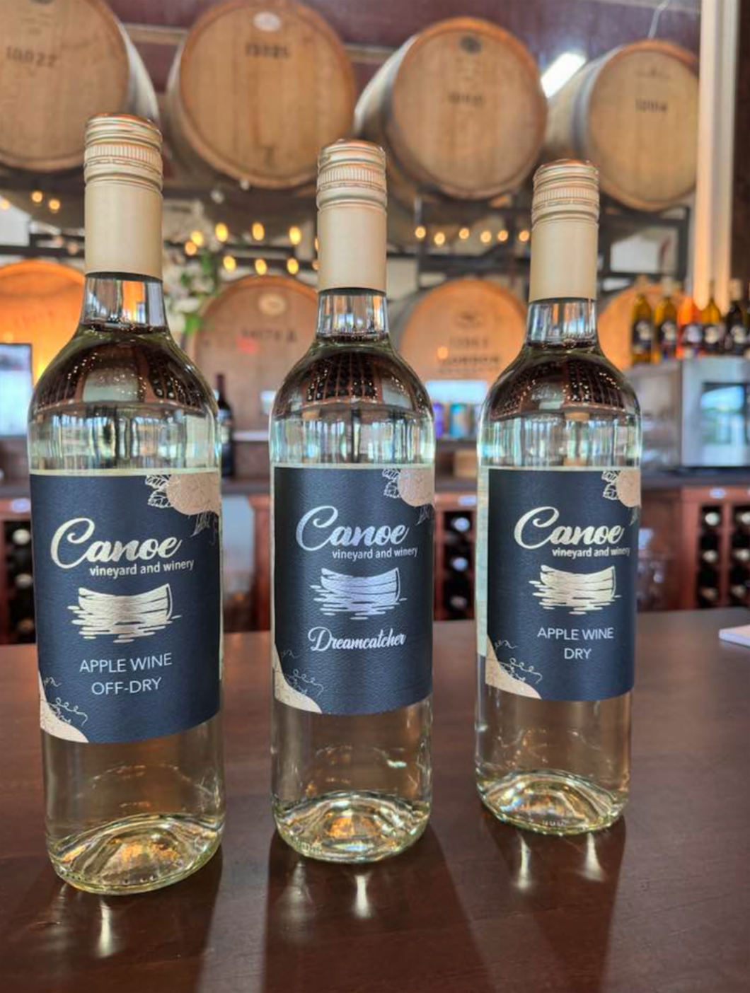 Three bottles of caneo apple wine are sitting on a wooden table.