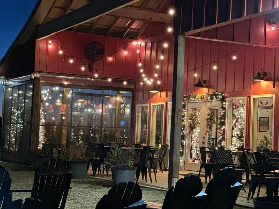 Red barn patio with string lights, tables, and chairs at dusk.