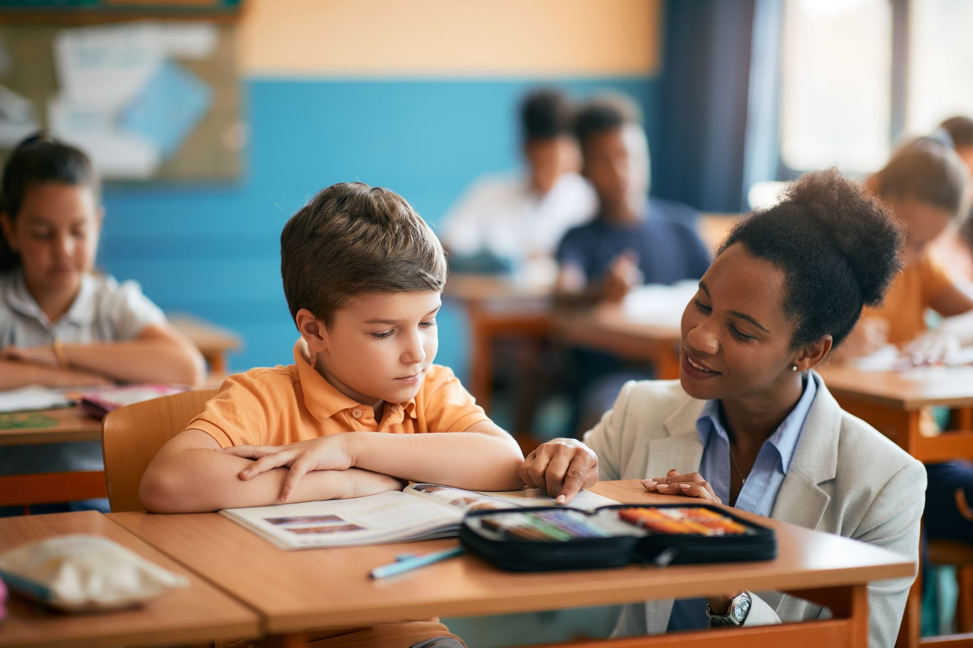 A teacher is helping a young boy with his homework in a classroom.