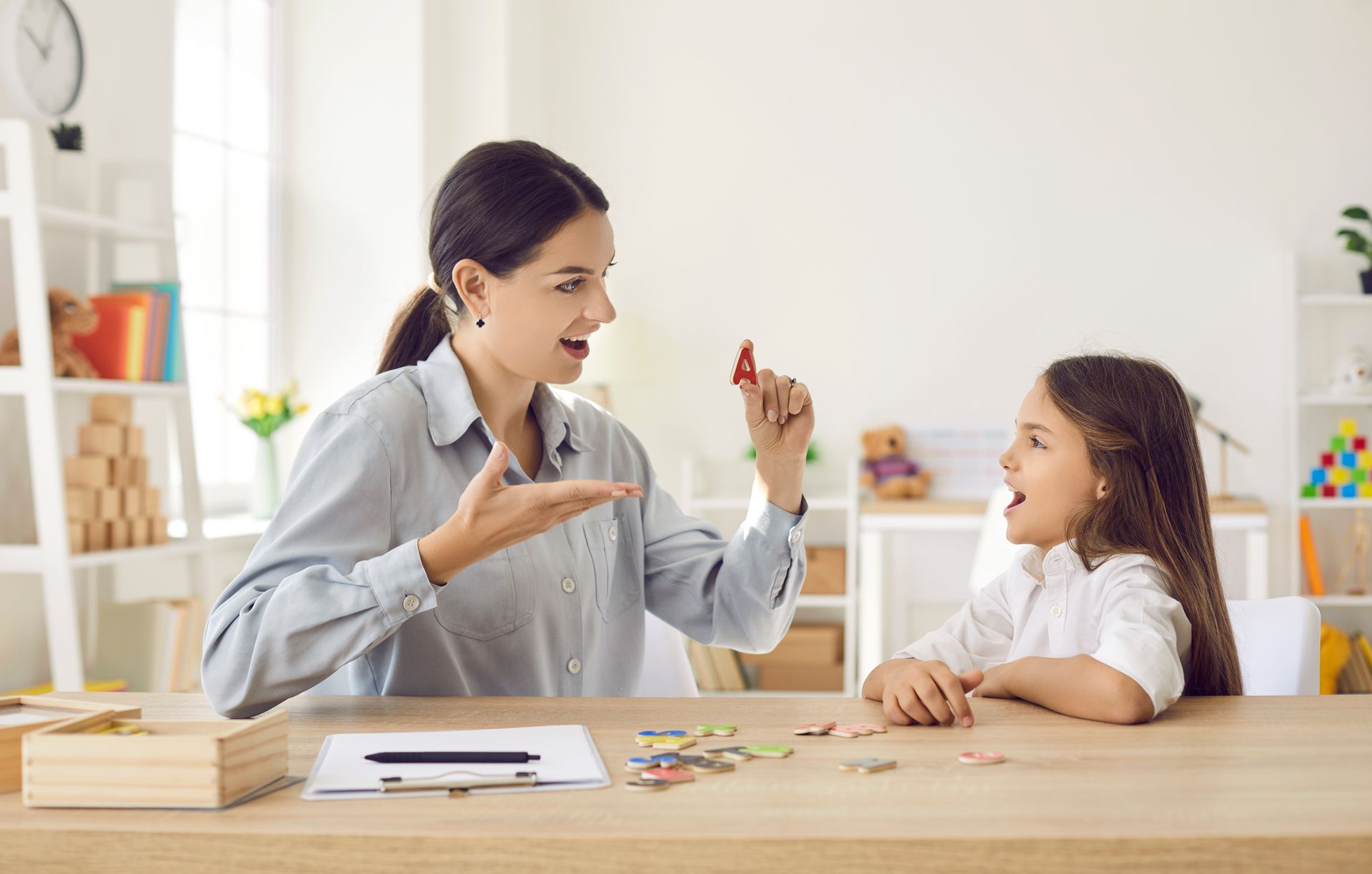A woman is sitting at a table talking to a little girl.