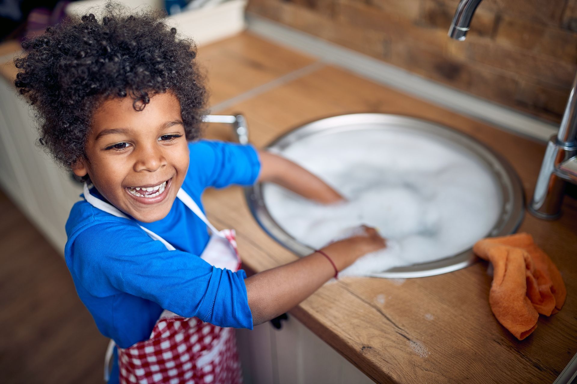 A young boy is washing dishes in a kitchen sink.