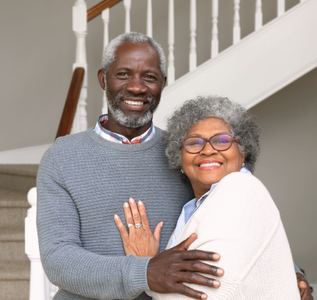 Smiling couple by a staircase, the woman with glasses, the man with a ring.