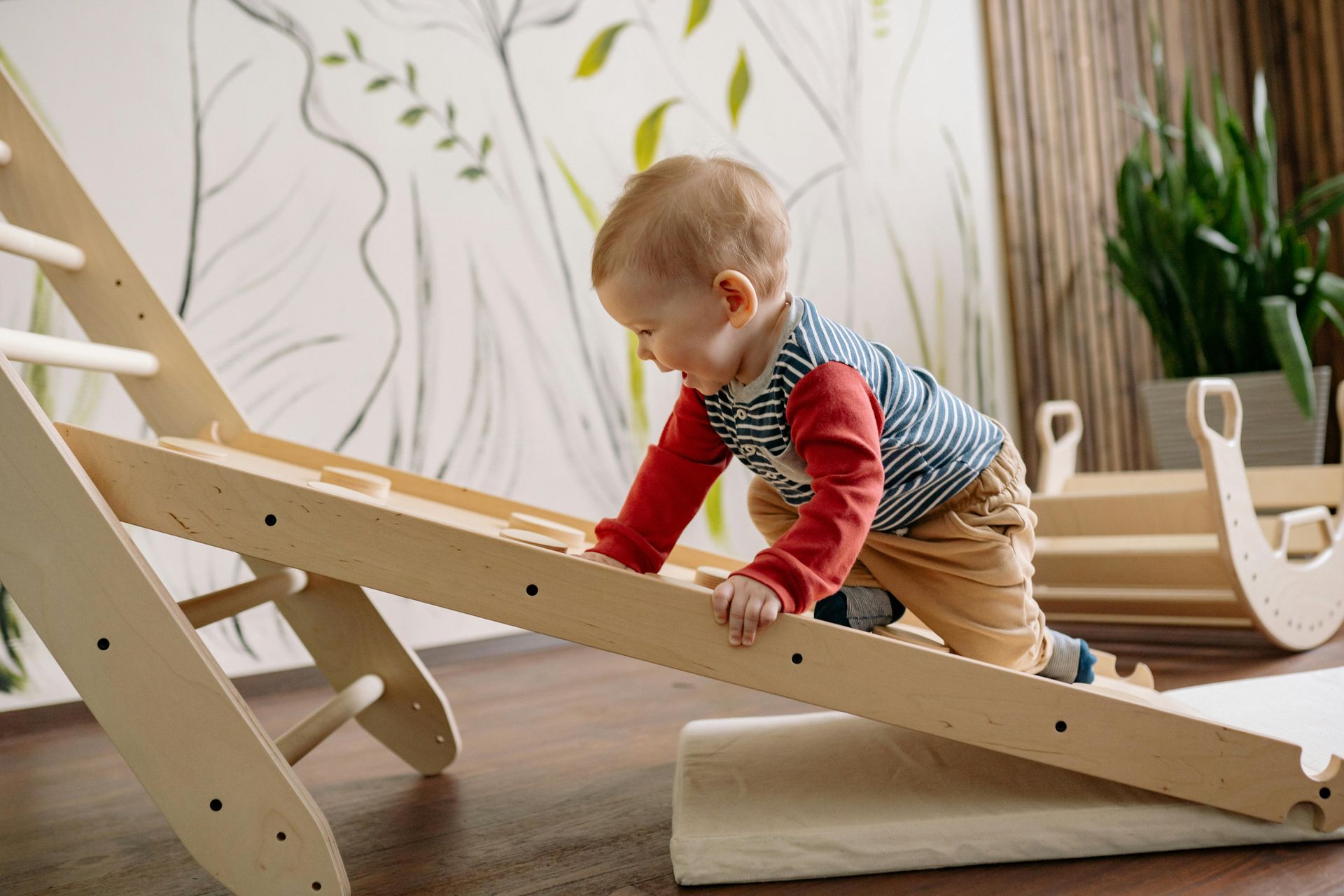 Toddler climbing on a wooden climbing frame, indoors in one of the rooms at Play's Kool Floreat Childcare Centre.