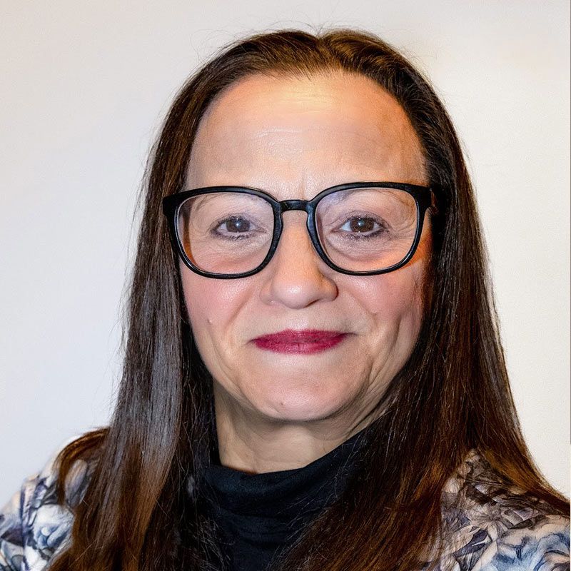 A woman wearing glasses and red lipstick is smiling for the camera.