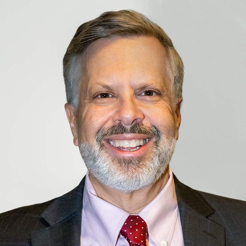 A man with a beard is wearing a suit and tie and smiling.