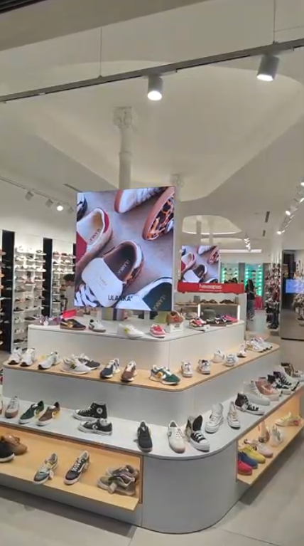 Interior de una zapatería con exposición de calzado y pantallas digitales que muestran imágenes de los productos.