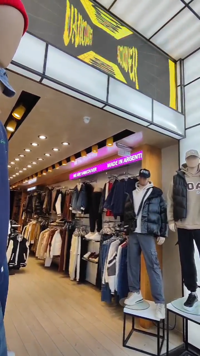 Interior de una tienda de ropa con maniquíes, percheros y letreros.