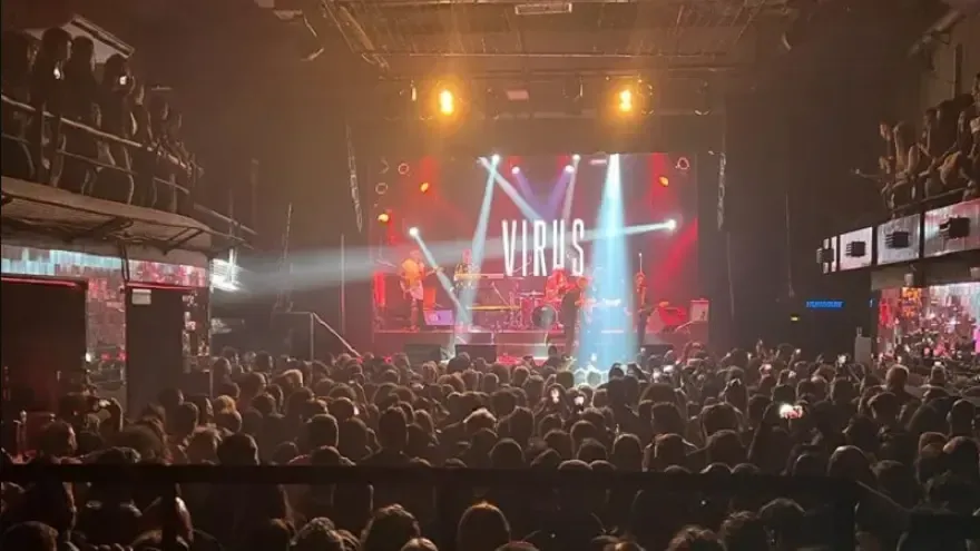 La banda actúa en el escenario de una sala de conciertos abarrotada, con luces brillantes 