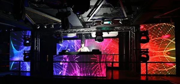 Un DJ actuando en un escenario con paneles LED de colores en un club.