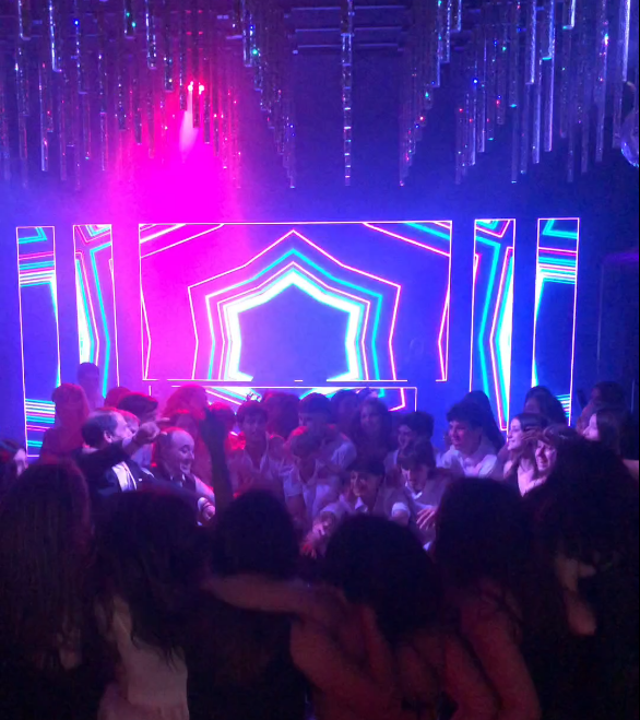 Escena de discoteca con una pista de baile abarrotada y una brillante iluminación de neón en el escenario.