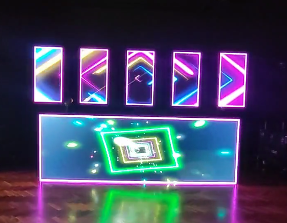 Escenario con patrones geométricos de neón en seis pantallas verticales y una gran pantalla horizontal.