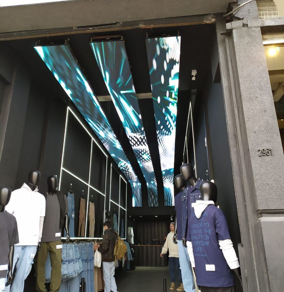 Escaparate con maniquíes, pantalla digital en el techo y clientes mirando ropa. Esquema de color blanco y negro.