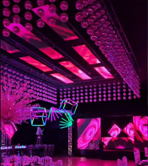 Espacio para eventos iluminado en rosa y morado con esferas colgantes, arte geométrico de neón y pantallas digitales.