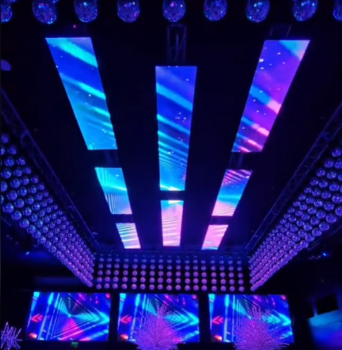 Escenario iluminado con paneles y luces LED azules y moradas en un recinto.