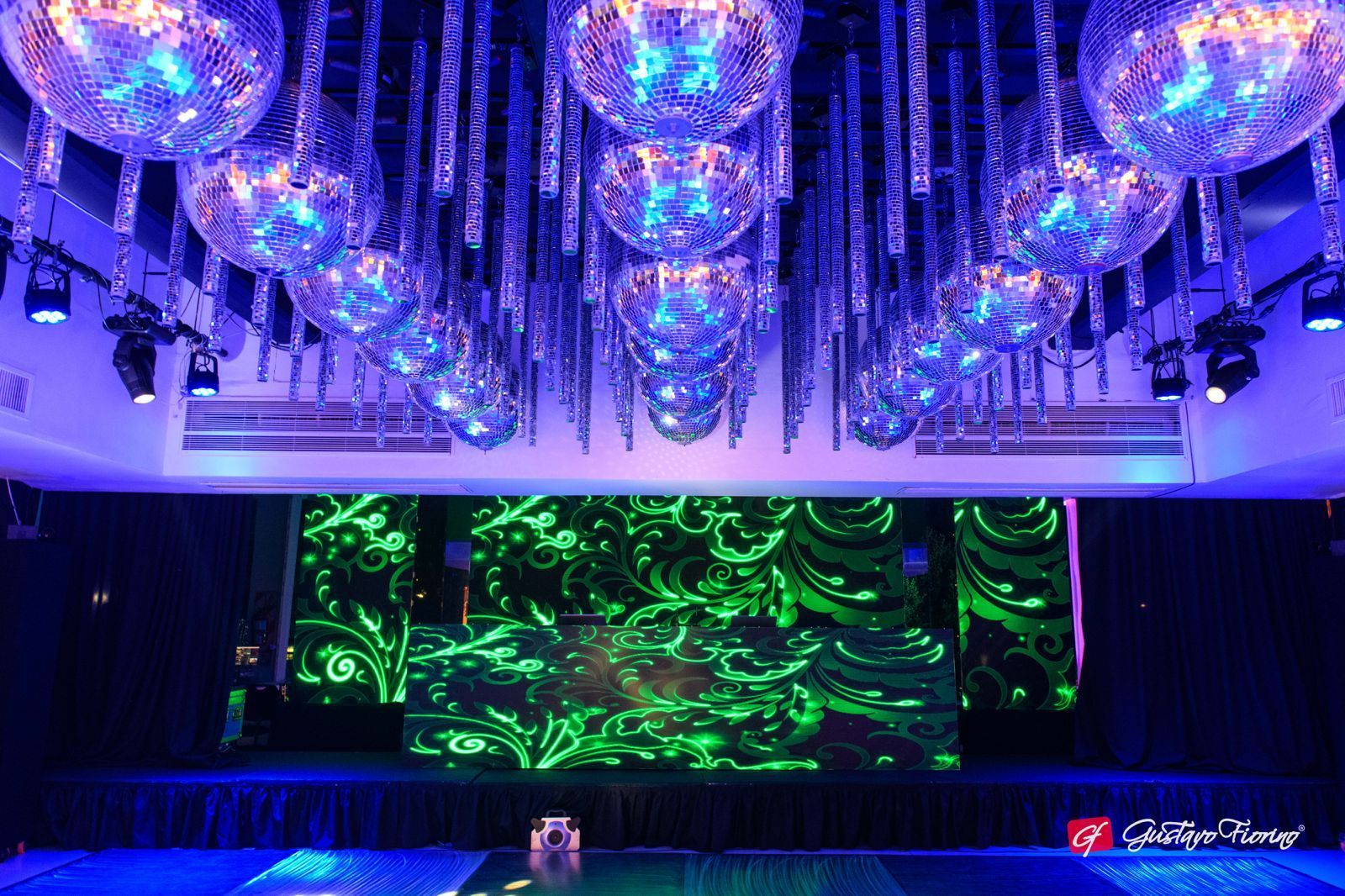 Discoteca con bolas de discoteca espejadas colgando del techo, escenario con luces de neón verdes.