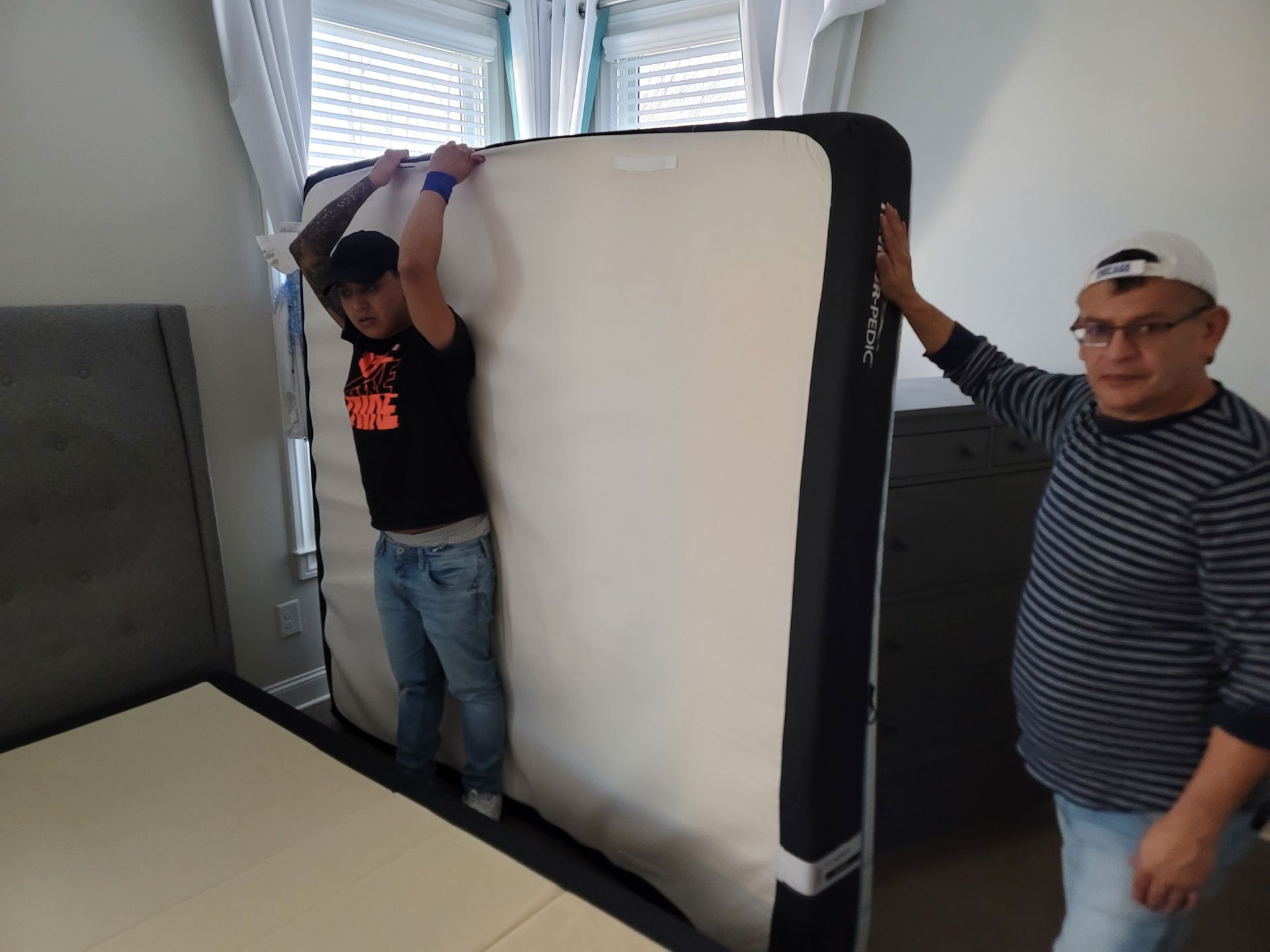 Two men are carrying a large mattress in a bedroom