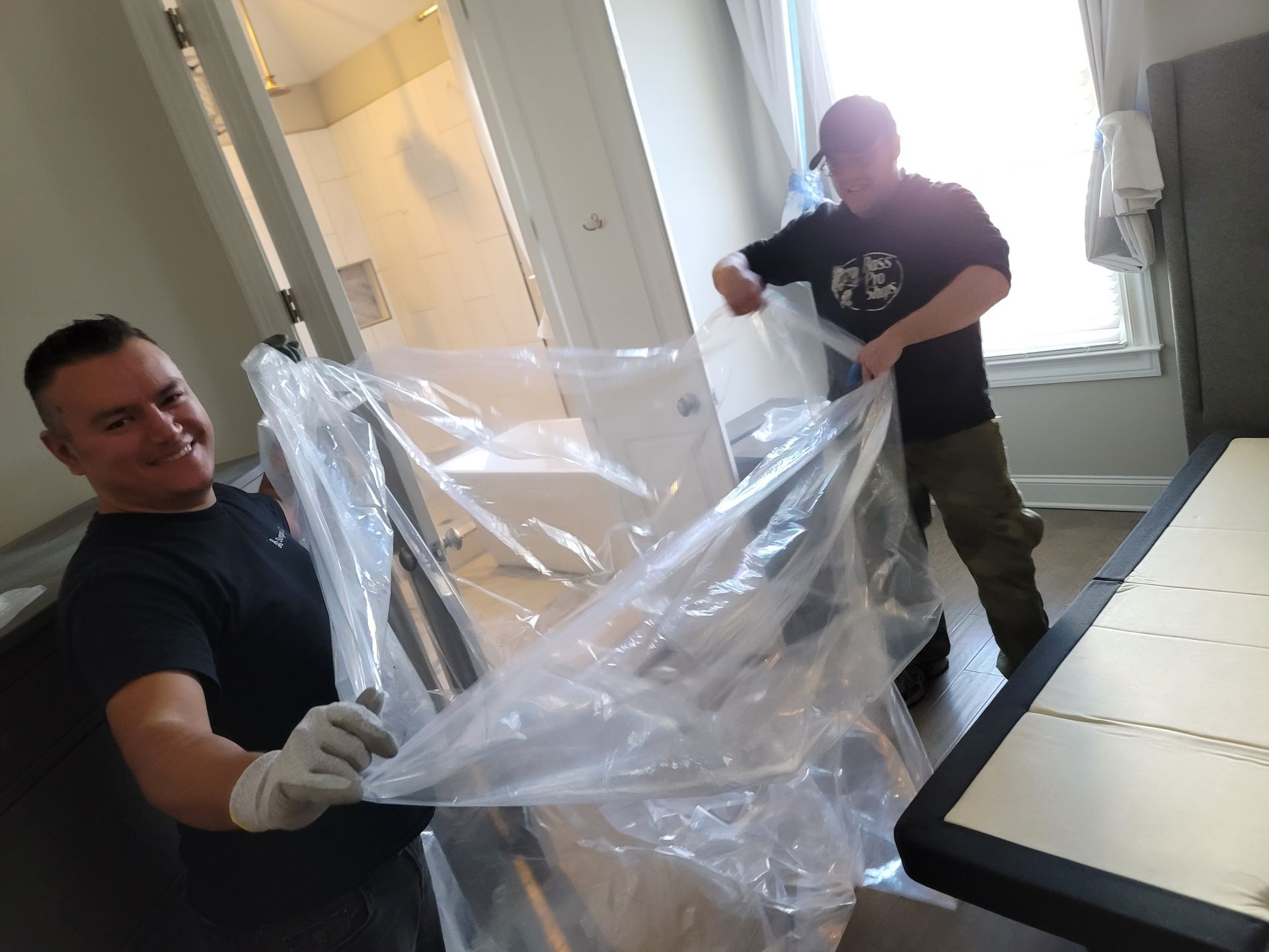 Two men are wrapping a refrigerator in plastic.
