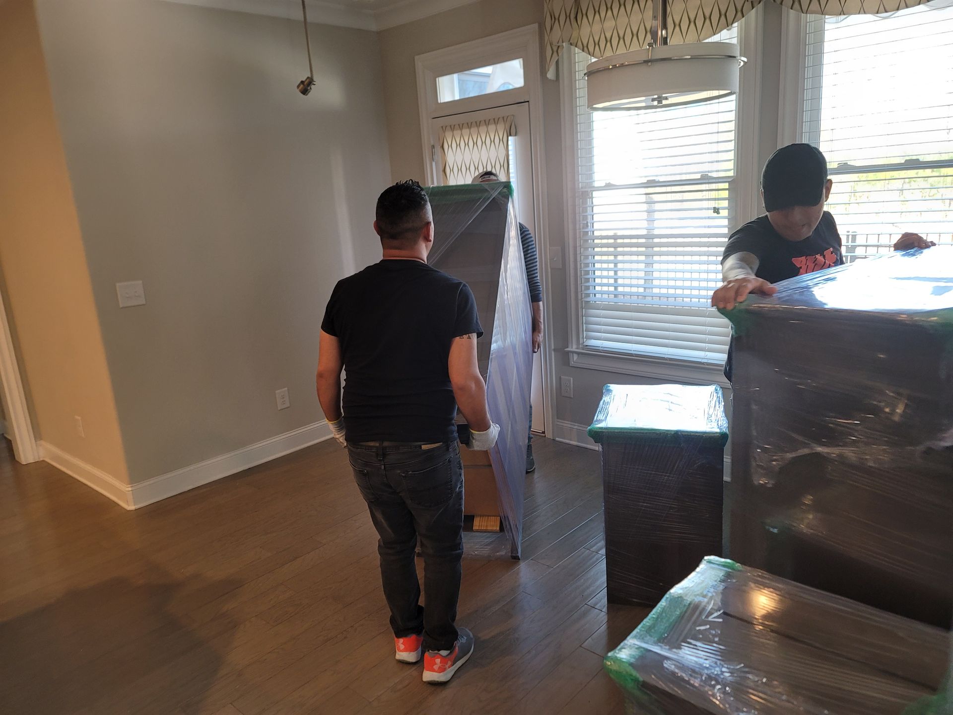 Two men are carrying a dresser in a living room.