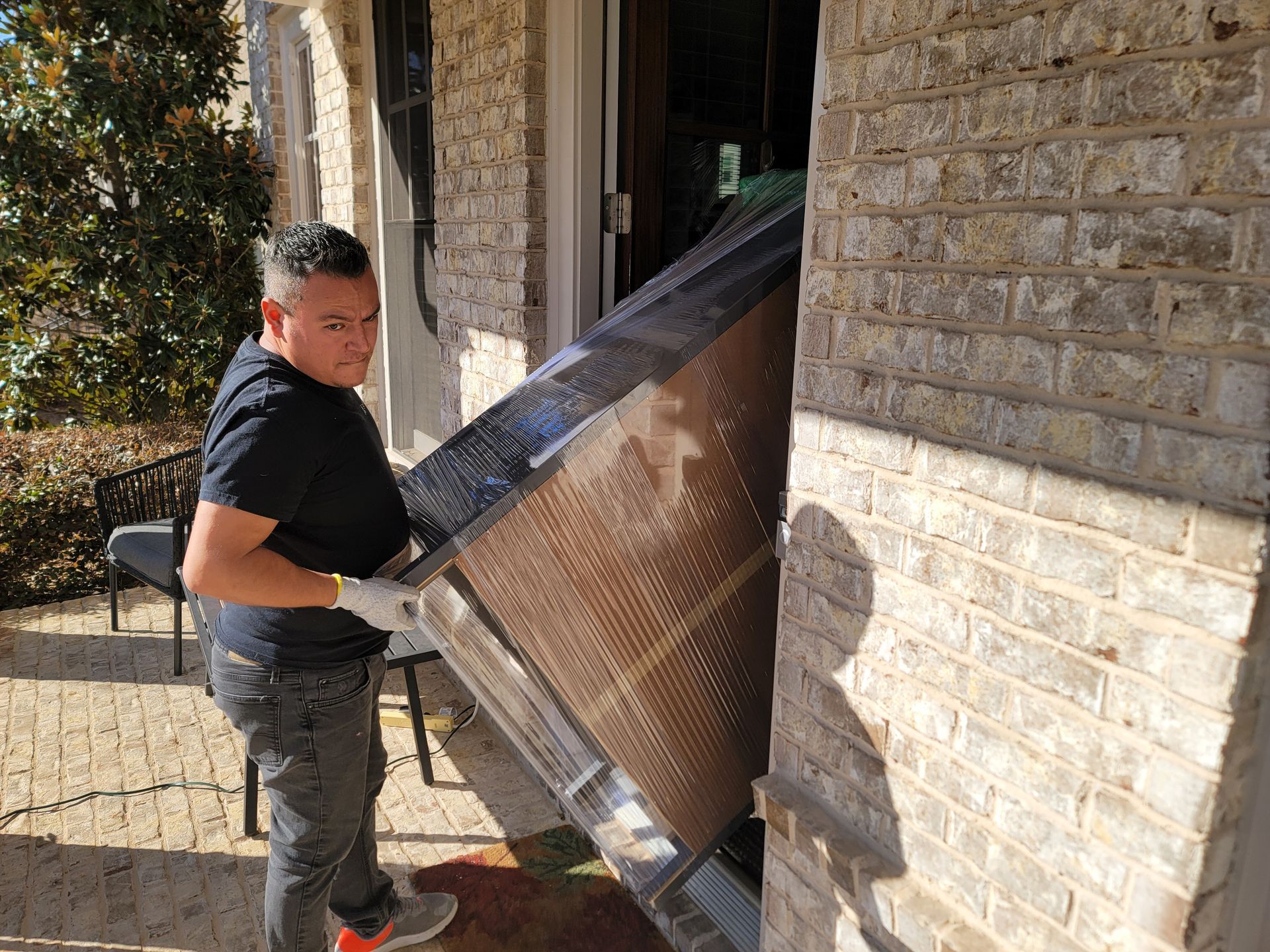 A man is carrying a piano in front of a brick building.