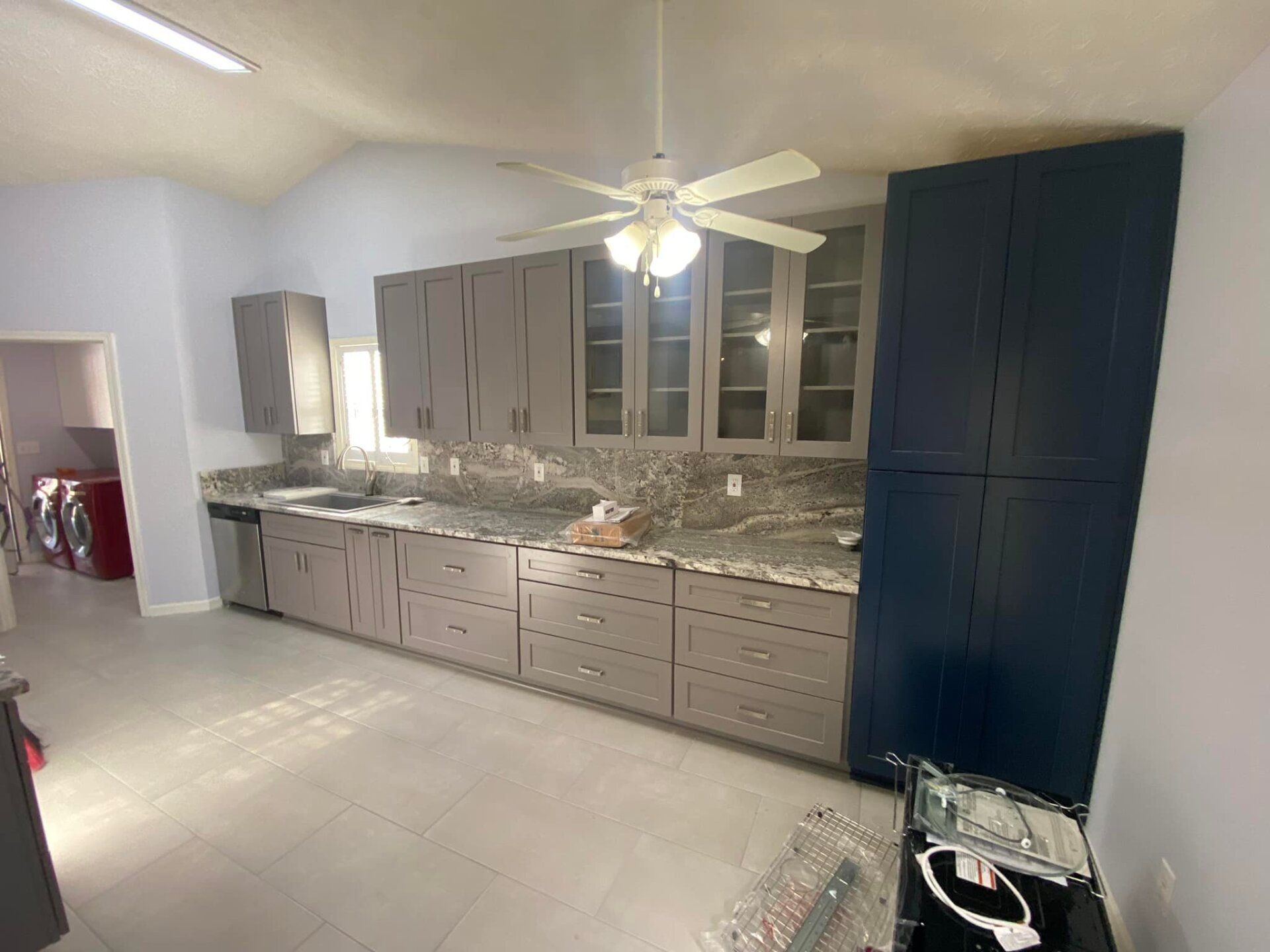 A kitchen with gray cabinets and blue cabinets and a ceiling fan.